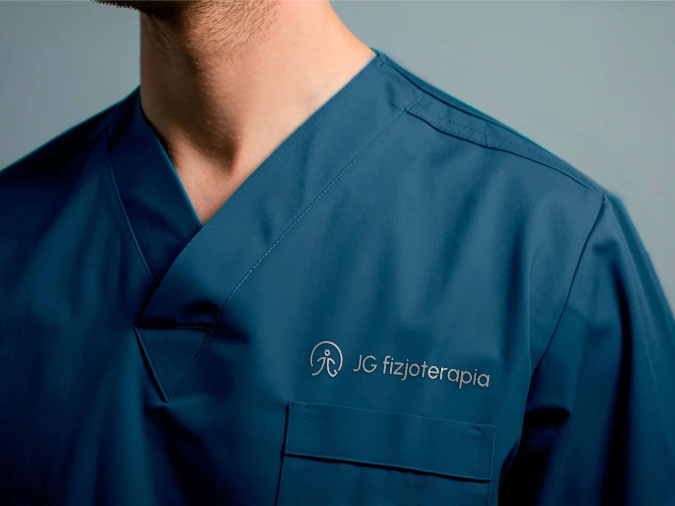 JG Fizjoterapia logo embroidered on a physiotherapist’s blue medical scrubs.